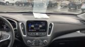 Driver-seated view of a car interior with the center touchscreen and climate controls, a sheet of paper on the dashboard, and a parking lot of cars visible through the windshield.