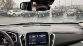 Driver's-eye view of a car interior on a rainy day; raindrops on the windshield, rearview mirror, and center touchscreen showing radio.