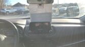View from the driver's seat showing the dashboard and steering wheel, with a piece of paper hanging from the rearview mirror and a parking lot outside the windshield.