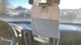 Blurry view inside a car showing a dashboard and rear-view mirror with parked cars outside the windshield.