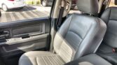 Interior of a car showing black leather front seats and seat belts, with a view of the parking lot outside through the open door window.
