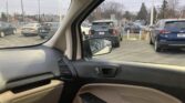 Car interior view with beige and black dashboard; outside a parking lot filled with SUVs and sedans visible through the window edge