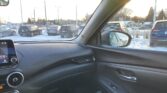 View from inside a car at a snowy parking lot; multiple parked SUVs visible through the windshield and side mirror (bright day)
