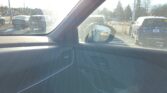 View from inside a car showing the dashboard and windshield, with a parking lot and other vehicles visible outside, bright sunlight causing glare.