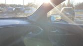 Bright sun glare through car window with lens flare over a snowy parking lot viewed from the front seat interior.