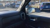 Interior view from a car, showing the passenger-side window and mirror with a dealership parking lot of parked cars beyond.