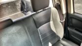 Black leather car rear seat with headrest, visible seatbelt buckled, and an open truck bed seen through the window behind the passenger.