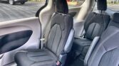 Interior of a modern SUV's second row with two black fabric captain's chairs, white stitching, and visible seat belts; outside parking lot seen through windows.