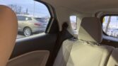 Interior of a car's backseat with beige fabric seats and headrest, view through the window shows a gray SUV parked in a lot outside.