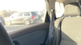 Backseat view inside a car, with a sunlit window showing parked vehicles outside and glare on the glass.