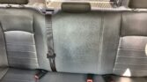 Rear car seat in black leather with three seat belts and a center headrest, view toward the trunk through the back window.
