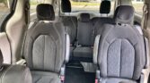 Interior of a dark fabric-cloth minivan with multiple rows of seats and white stitching, showing headrests and aisle down the middle.