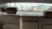 View from the back seat of a car looking out the rear window at a dealership with a green-roofed building and parked cars outside