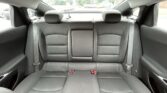 Rear car seat view: three black fabric seats with headrests and visible seatbelts in a dark interior.