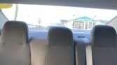 View of the car's rear seating area with three black headrests and a seat belt, looking toward the back window and a building outside with a green roof.