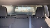 View from the back seat of a car facing the rear windshield; three headrests, a center seat belt, and a stickered rear window with parking lot outside visible behind glass.