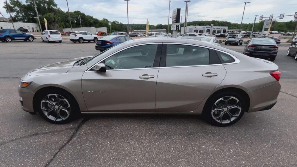 Silver Chevrolet Impala sedan viewed from the side in a car dealership lot, with other vehicles in the background.