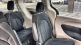 Back seat area of a car with black cloth seats and white stitching; parking lot visible through the windows outside.