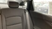 Back seat of a car with gray fabric upholstery, headrest, and a folded seat belt, viewed through a rain-speckled window.