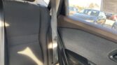 Rear car seat with black upholstery and a hanging center seat belt; outside right-side window, parked cars are visible in bright daylight.
