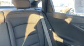 Back seat of a car with black fabric upholstery, visible headrest, and a vertical seatbelt near the window; sunlight casts shadows on the seat backrest.