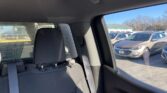 Back seat of a car with two headrests and a seat belt; outside, a row of parked cars at a dealership lot visible through the window.