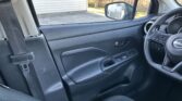 Driver-side interior of a Nissan, showing the steering wheel, door panel with window controls, and a seat with a visible seatbelt buckle; window and side mirror in view.