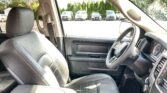 Interior of a right-hand-drive car photographed from the back seat, showing the front seats, center console with cup holders, and steering wheel, with a parking lot outside through the windows.
