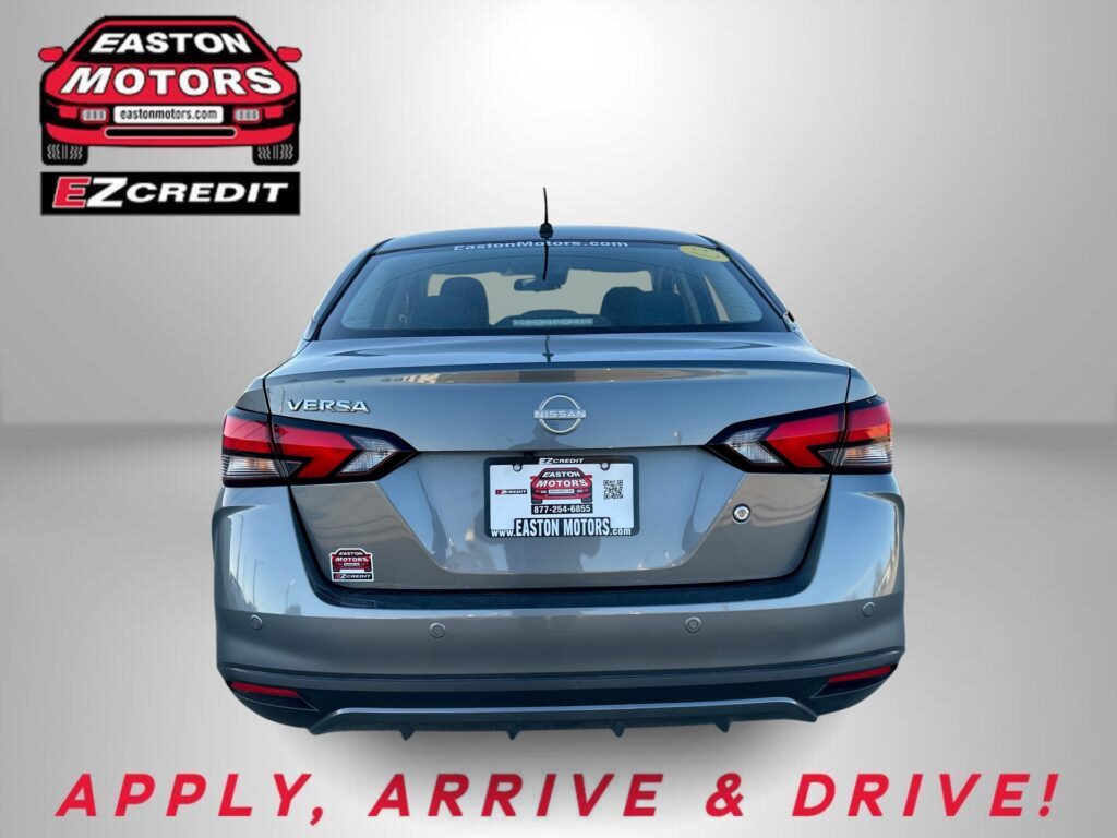 Rear view of a silver Nissan Versa with Easton Motors branding on a light gradient backdrop and part of the 'APPLY, ARRIVE & DRIVE!' slogan visible at bottom.