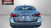 Rear view of a silver Nissan Versa with Easton Motors branding on a light gradient backdrop and part of the 'APPLY, ARRIVE & DRIVE!' slogan visible at bottom.