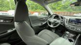 Front interior of a Chevrolet SUV, showing the steering wheel, dashboard, and dark fabric seats from the back seat view outside the door window.