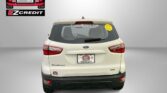 Rear view of a beige Ford SUV with EZCredit branding on the back window and a smiley sticker on the right window; dealership ad background shows 'APPLY, ARRIVE & DRIVE!' text at bottom.