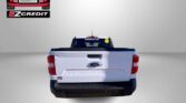 Rear view of a white Ford Maverick pickup with dealership logo in the top-left and the slogan 'APPLY, ARRIVE & DRIVE!' in red at the bottom.
