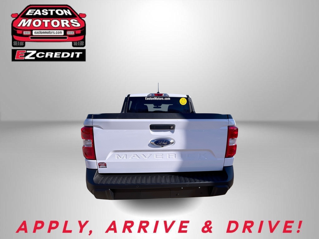 Rear view of a white Ford Maverick pickup with dealership logo in the top-left and the slogan 'APPLY, ARRIVE & DRIVE!' in red at the bottom.