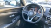 Blurry interior of a car showing the steering wheel and dashboard, with a side mirror and a busy parking lot outside the windshield.