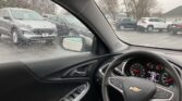 Driver's-seat view of a car interior on a rainy day, raindrops on the windshield and a dashboard with a Chevrolet emblem visible.