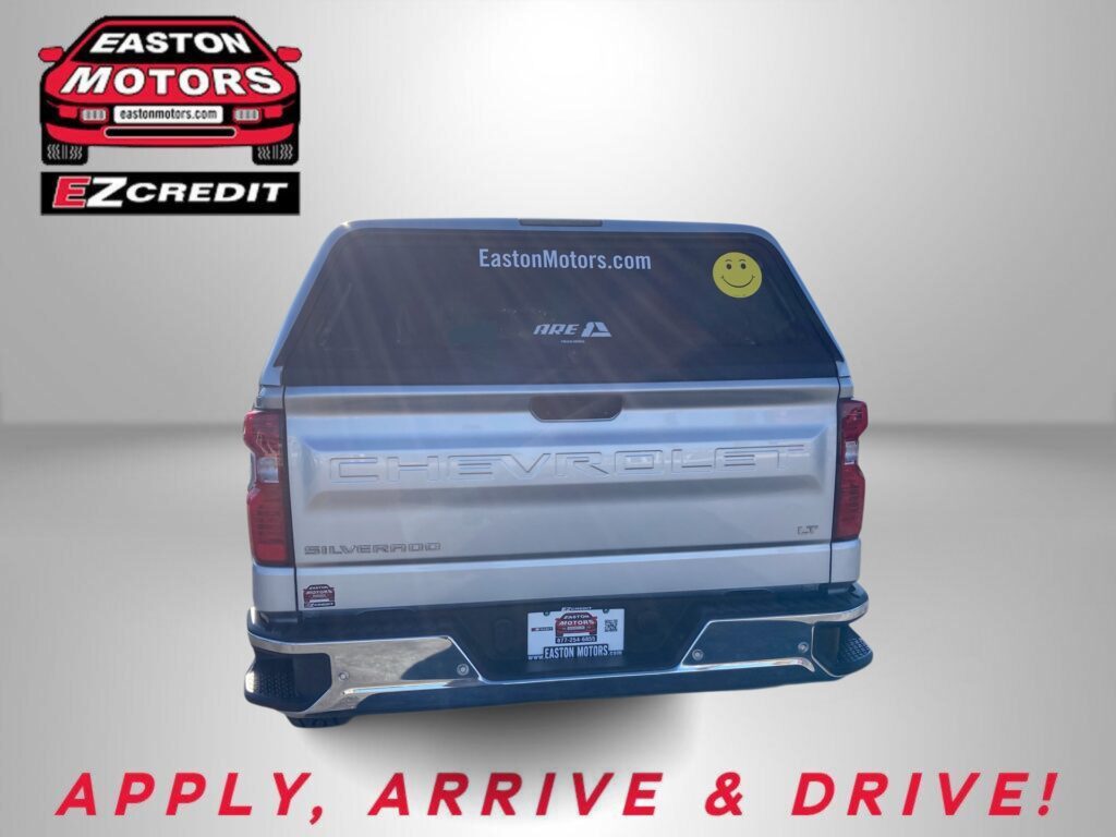 Rear view of a silver Chevrolet Silverado with a yellow smiley decal on the rear window and the 'Easton Motors' logo in the upper left; large red 'APPLY, ARRIVE & DRIVE!' text at bottom.