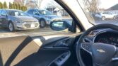 Driver’s view from inside a Chevrolet, showing the steering wheel with logo and a parking lot of silver and white SUVs outside the window.