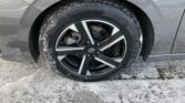 Close-up of a Nissan alloy wheel with a snow-dusted tire on a gray car, showing the brake components behind the rim.