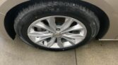 Close-up of a car tire and silver alloy wheel, showing tread and wheel well of a beige vehicle on pavement