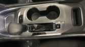 Front center console of a car with two circular cup holders, gear selector to the left, and an electronic parking brake button nearby.