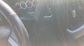 Interior car view with steering wheel in foreground and blurred instrument cluster seen through the windshield due to glare and reflections, obscuring details.