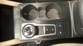 Center car console with two circular cup holders, a rotary gear selector, and nearby control buttons on a brushed-metal surface.