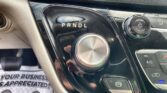 Close-up of a car's gear selector panel showing PRNDL with a blue indicator light on the dashboard area, glossy black finish nearby.