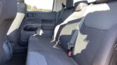 Back seat of a car with gray fabric upholstery, showing a three-seat bench, headrests, and visible seat belts in sunlight.