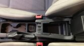 Center console of a car interior with cup holders and red seat belt buckles between front seats