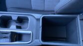 Center console in a car showing cup holders, storage bin, and part of the gear selector with a red 'PRESS' seatbelt buckle nearby.
