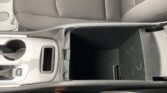 Center console of a car with an open storage cubby and two cup holders beside it, surrounded by black upholstery.