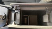 Open car center console showing an empty storage cubby and surrounding control area, including a circular dial on the left and a red seat belt buckle at bottom.