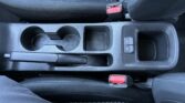 Center console of a car with two cup holders, a handbrake lever, and seat belt buckles visible between the seats.